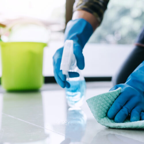 Husband housekeeping and cleaning concept, Happy young man in blue rubber gloves wiping dust using a spray and a duster while cleaning on floor at home.